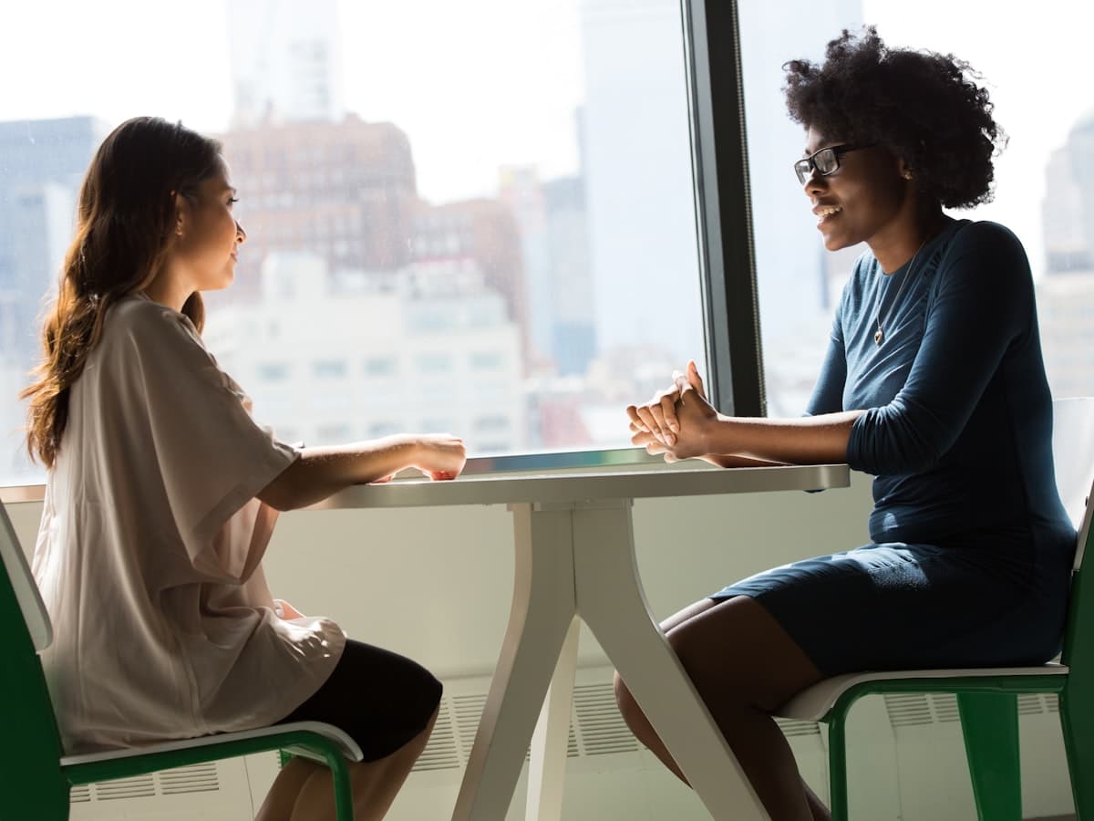 Two women talking across a table in a bright consulting room